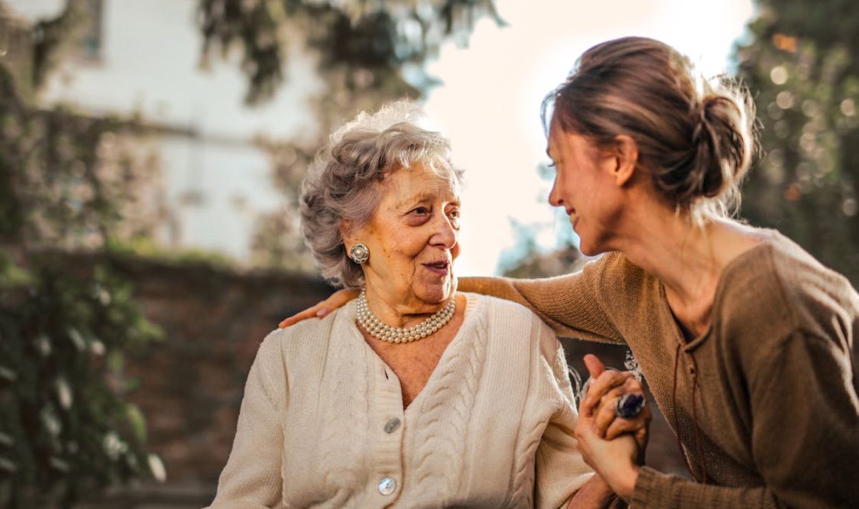 Elderly woman and adult daughter share a joyful, affectionate moment in a sunny garden.