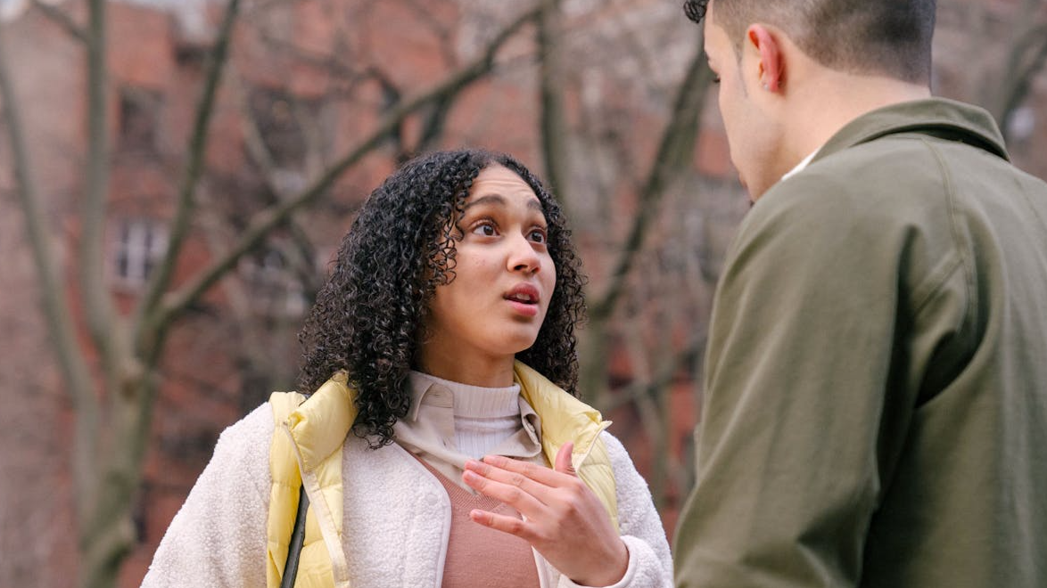 A young couple engaged in a serious conversation on a city street with trees in the background