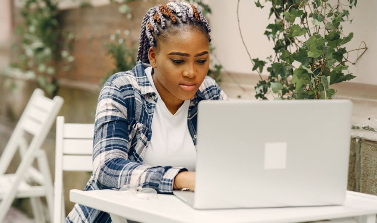 Young woman with colorful braids using a laptop outside at a white table
