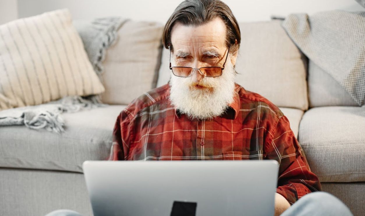 Senior adult man using a laptop while sitting on a couch in a cozy living room setting
