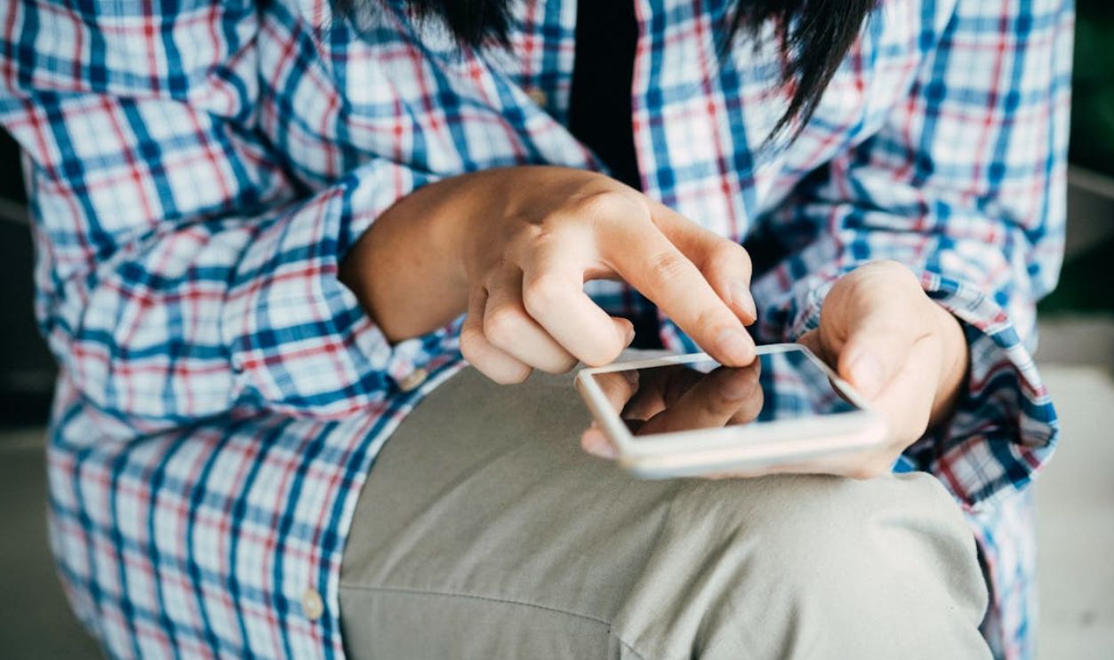 Woman's hands using a smartphone, wearing plaid shirt, indoors. Close-up shot highlighting touch interaction