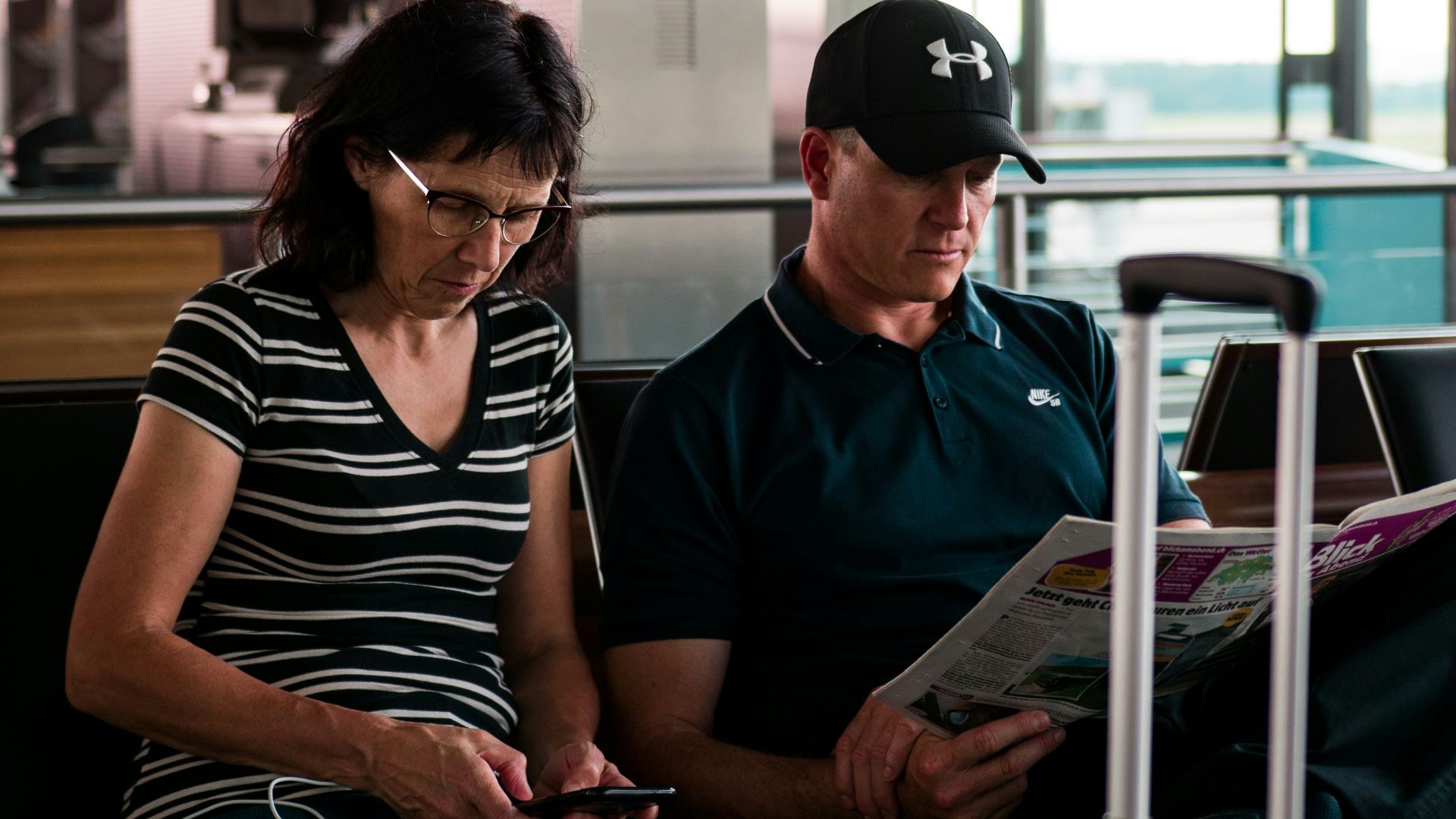 woman fiddling on smartphone beside man with cap reading newspaper