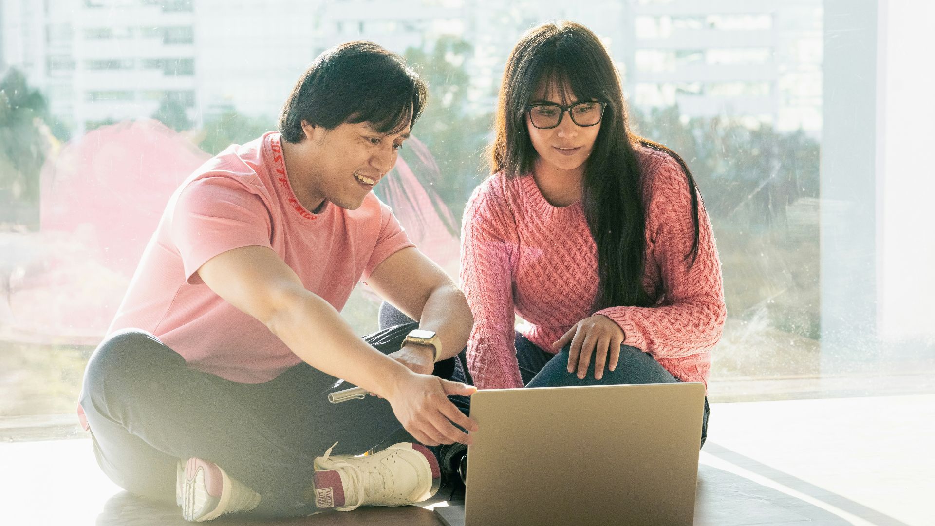 A man and woman sitting on the floor looking at a laptop