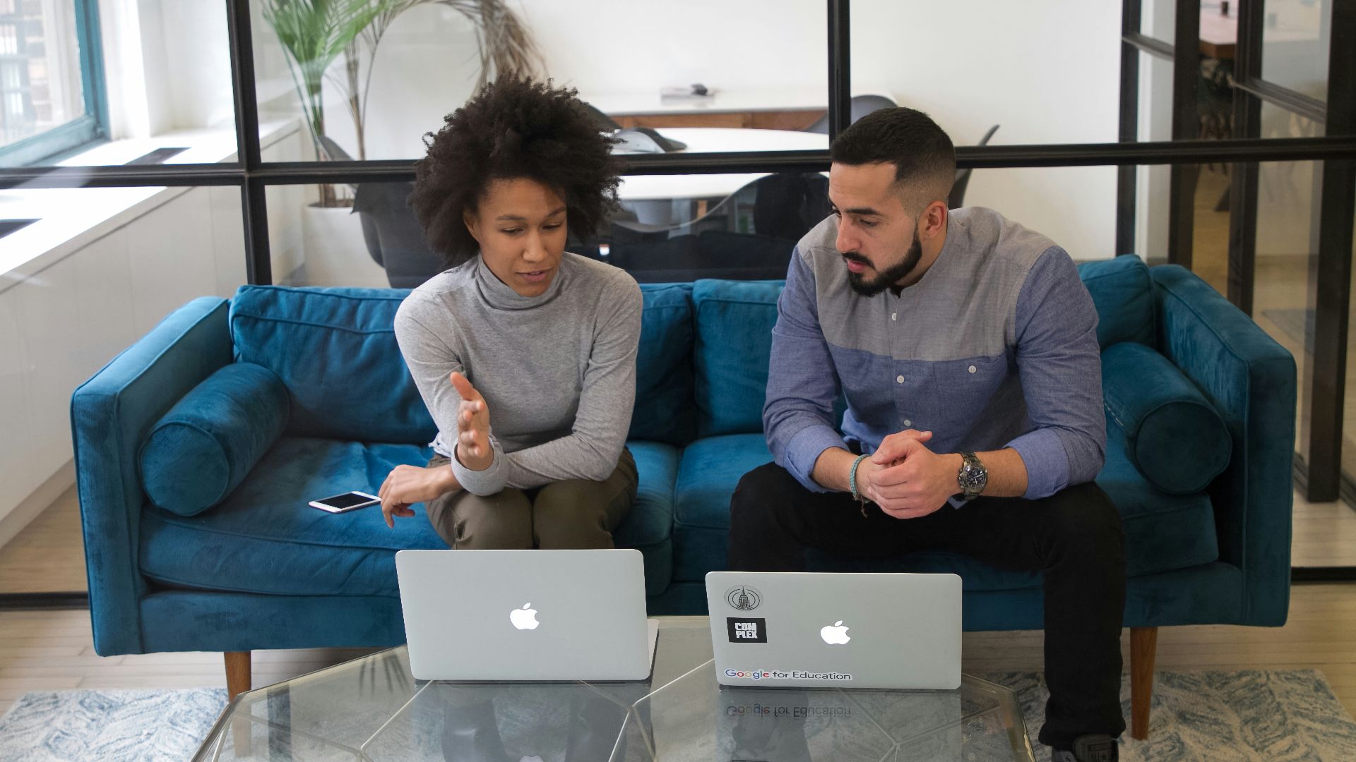 a man and woman sitting on a couch with their laptops