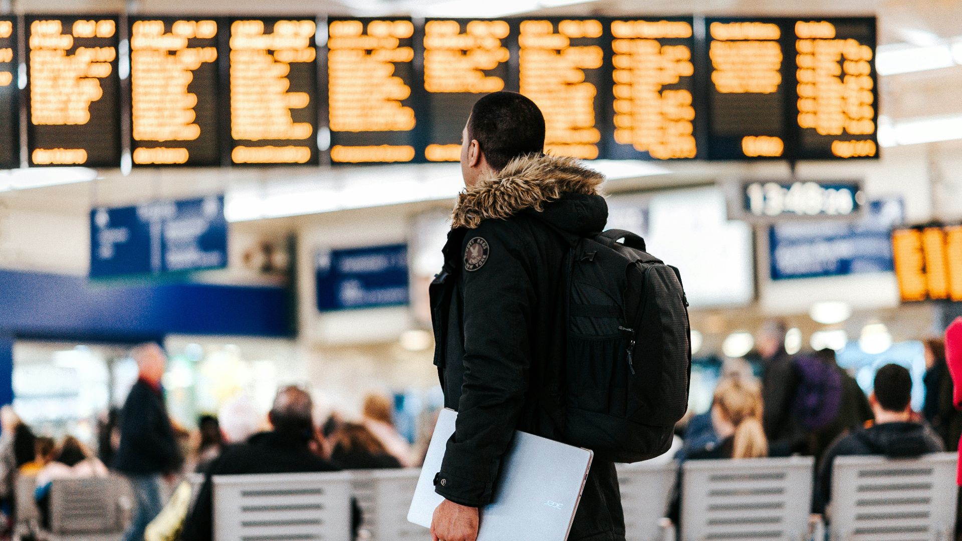 man standing inside airport looking at LED flight schedule bulletin board