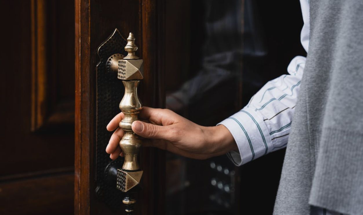 Close-up of a hand turning an ornate brass door handle, showcasing elegant craftsmanship