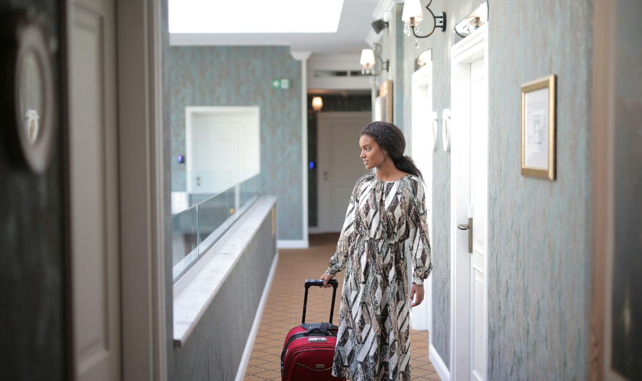 A woman walks with luggage through a stylish hotel corridor, embodying travel elegance.