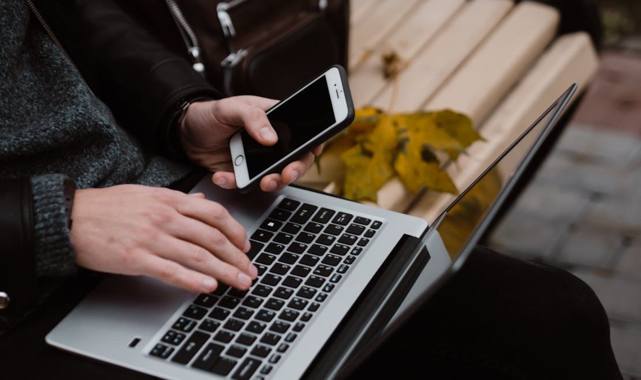Person working remotely using a laptop and smartphone outdoors, embodying digital nomad lifestyle