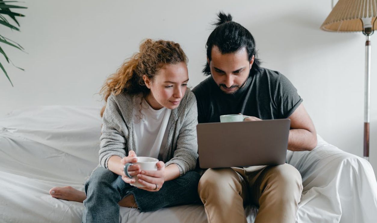 Young couple drinking coffee and browsing a laptop in their living room, enjoying their leisure time.