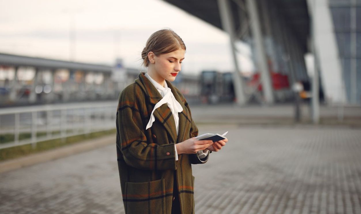 Confident young woman at an urban station with a trendy coat, preparing for travel.