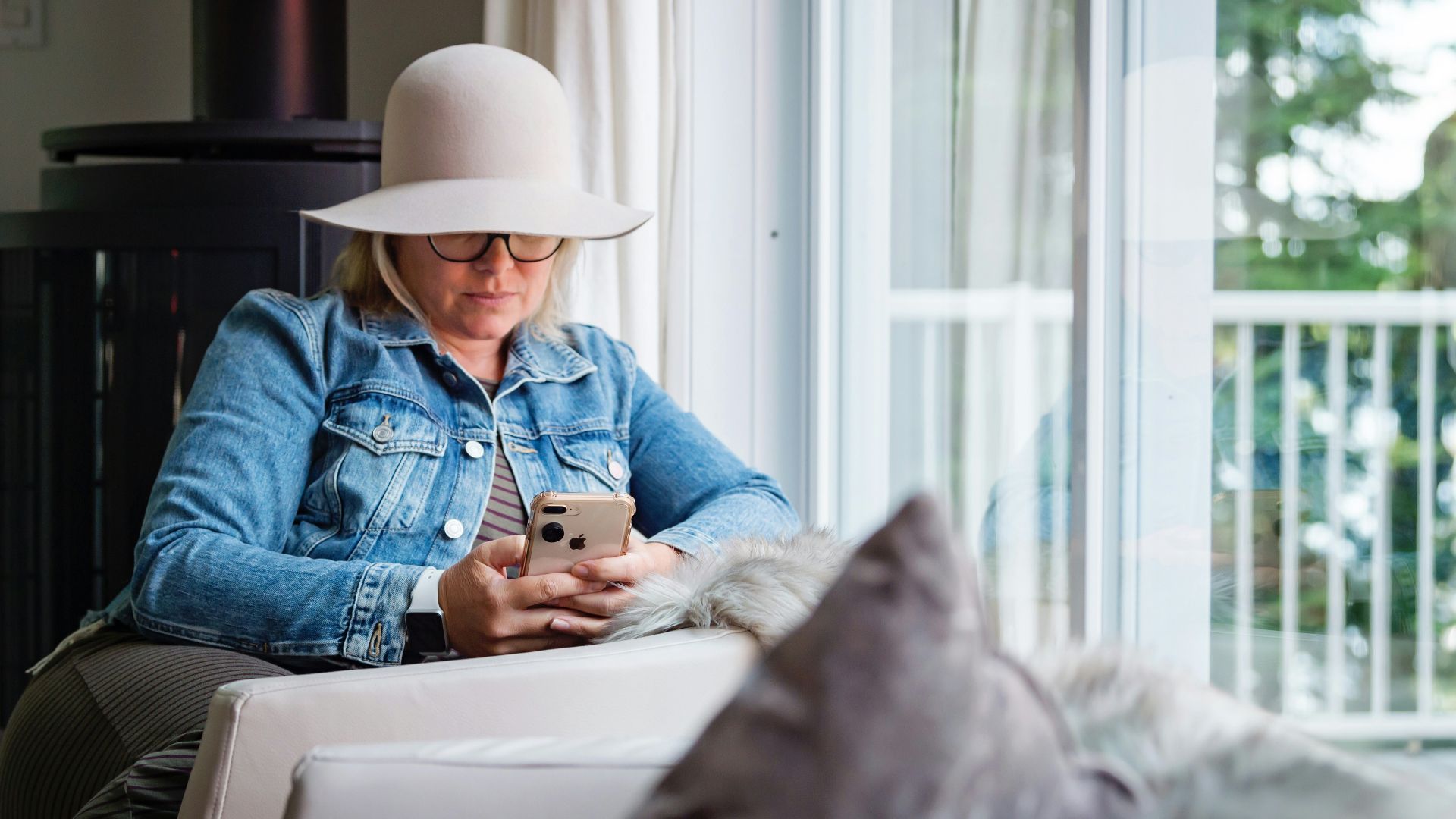 woman in blue denim jacket and gray hat sitting on white chair