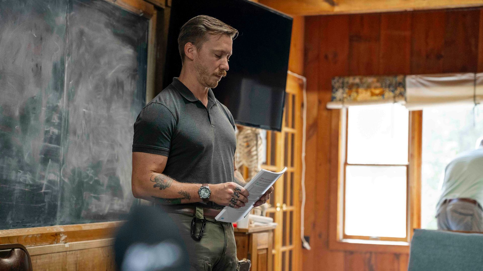 Man in polo shirt reading papers in room