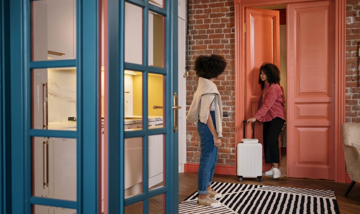 Two women with luggage in a stylish apartment hallway, getting ready to travel.