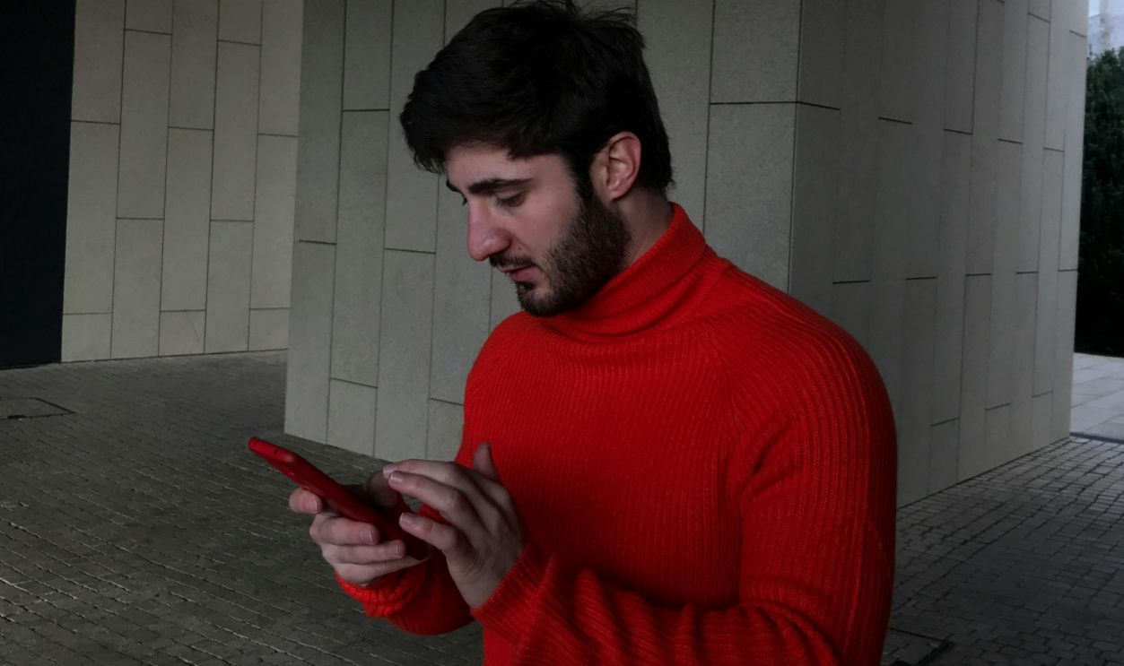 Young man in a red sweater focused on his smartphone in an urban environment