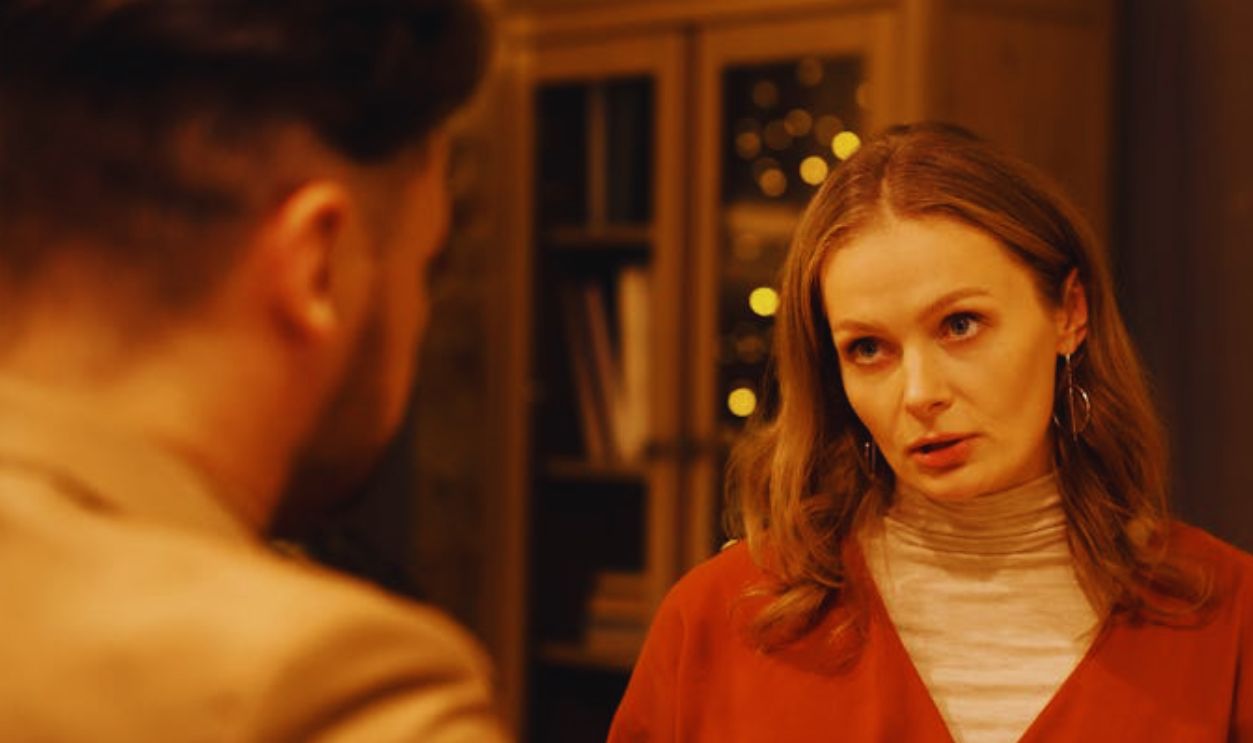 Three people enjoying a festive dinner table conversation surrounded by warm holiday lights