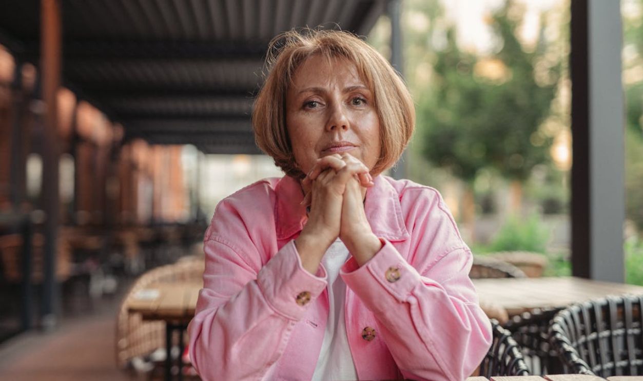 Portrait of a senior woman in pink, sitting outdoors in a contemplative pose
