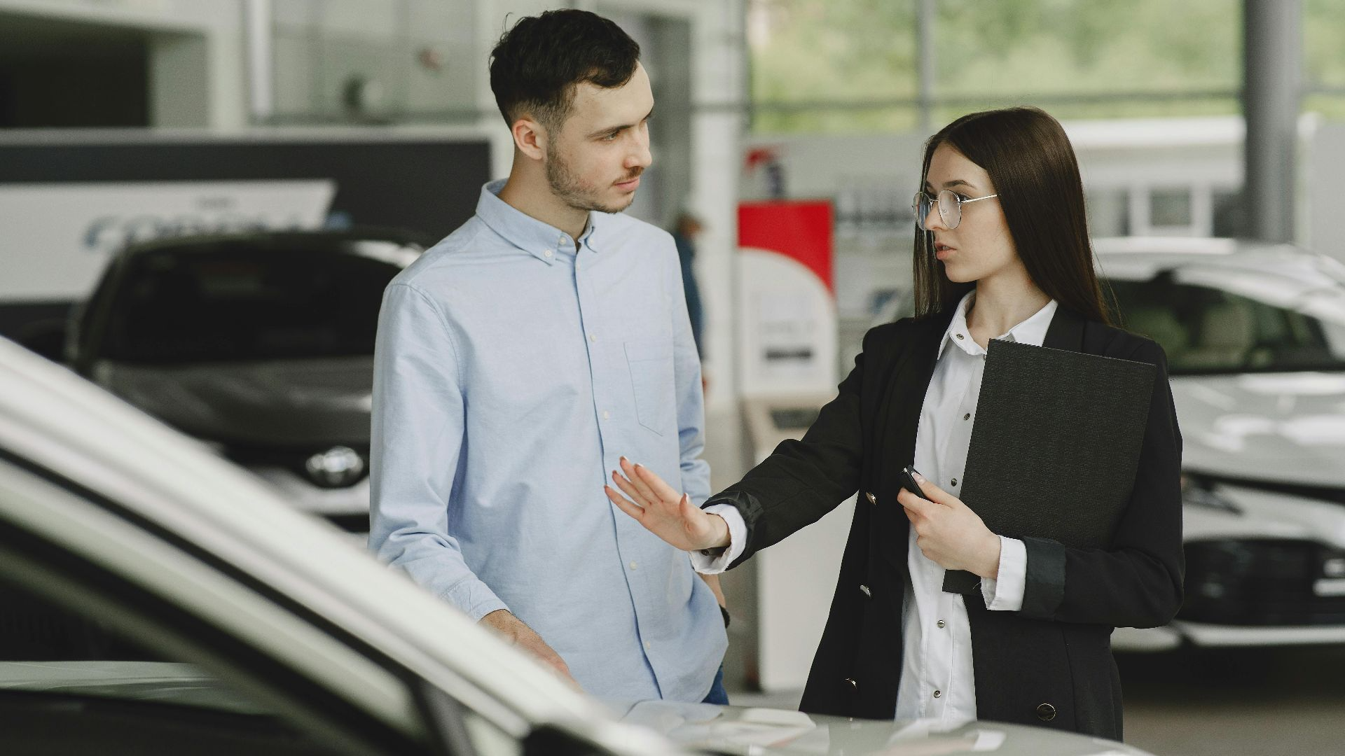 A salesperson and customer discussing car features in a dealership setting