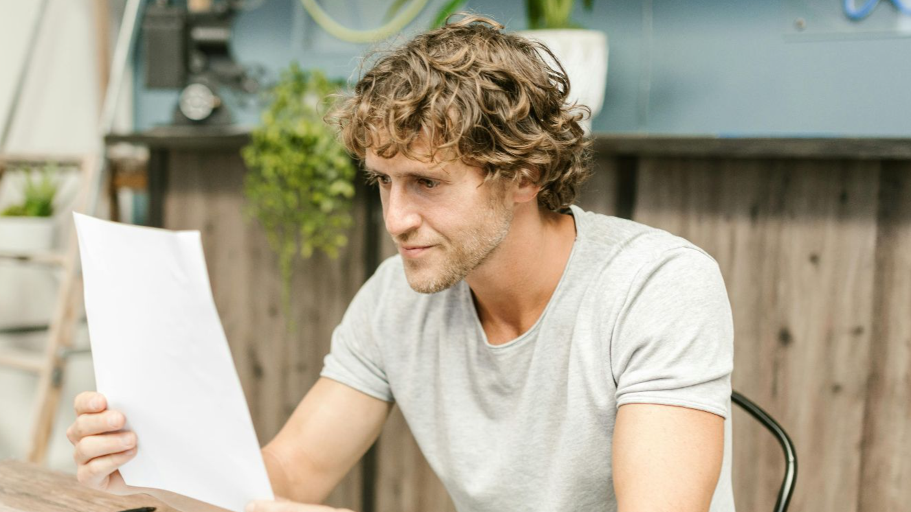 A man with curly hair evaluates documents at a desk, highlighting focused work in a professional setting
