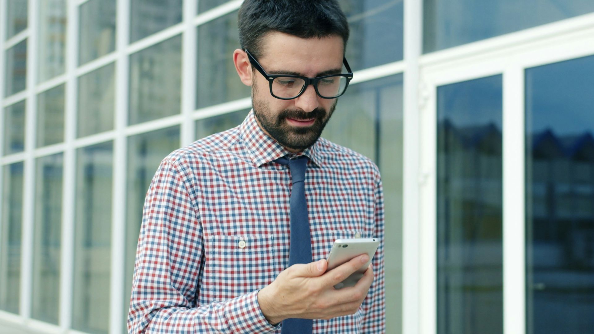Man in glasses looking at his phone outside building