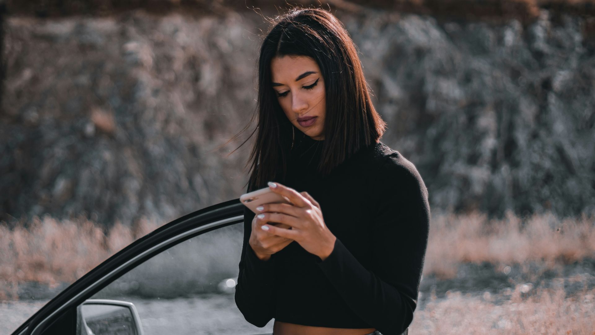a woman standing next to a car looking at her cell phone