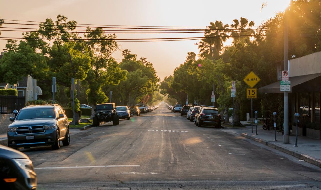 Sunset view of a tranquil urban street with parked cars and lush green trees