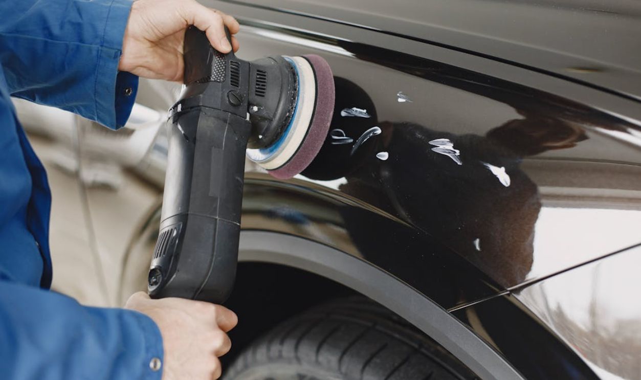 Hands using a polishing machine on a car's surface in a garage setting
