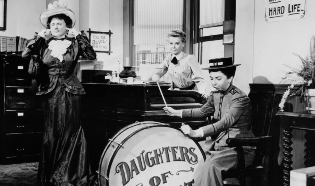Marjorie Main plugs her ears while Vera-Ellen sits at a desk and Alice Pearce plays a giant drum in a scene from the film 'The Belle Of New York', 1952. 