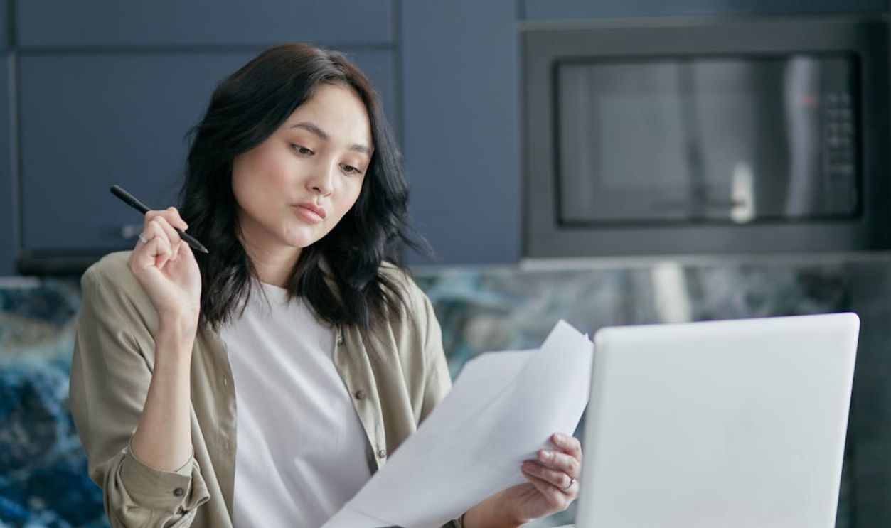 Young woman reviewing documents and working on a laptop in a modern home office setting