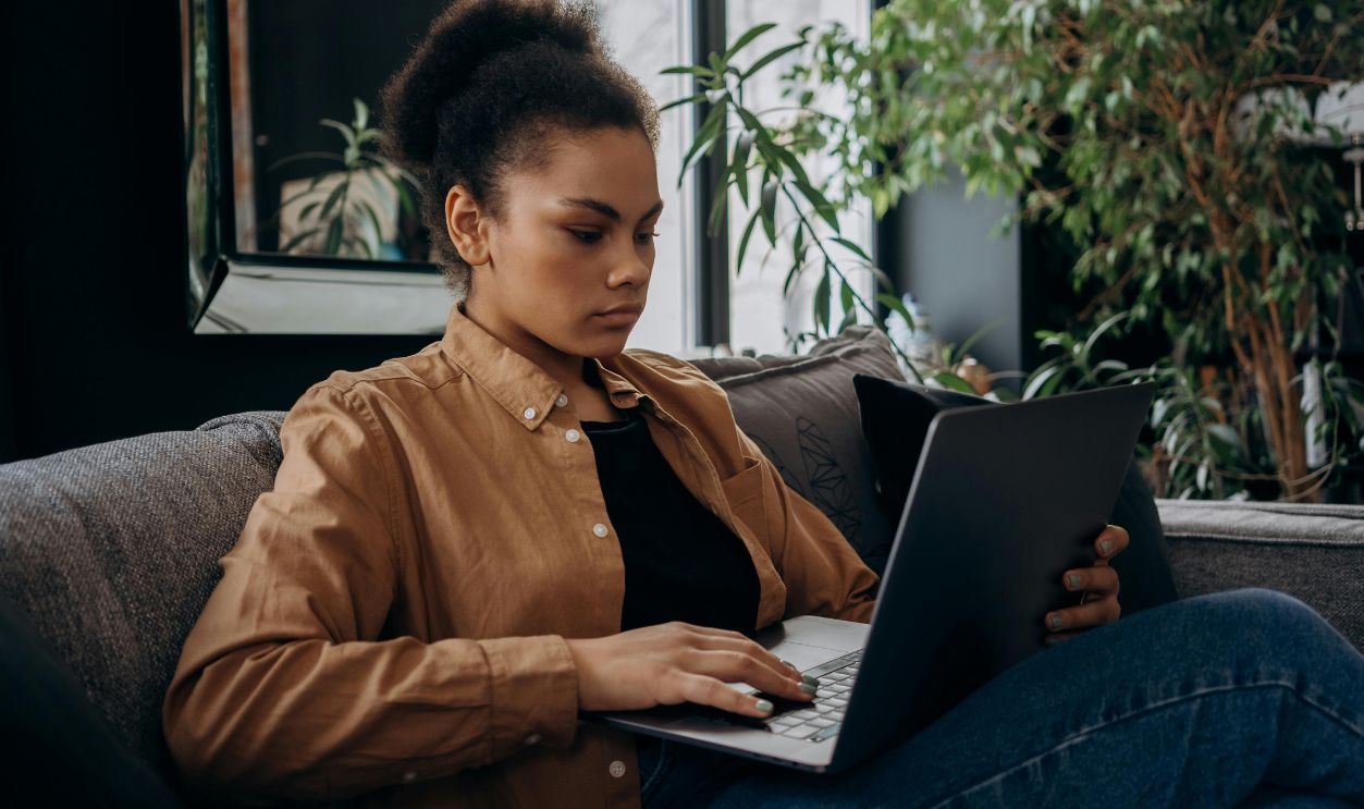 Focused young woman using a laptop on the couch, working remotely indoors