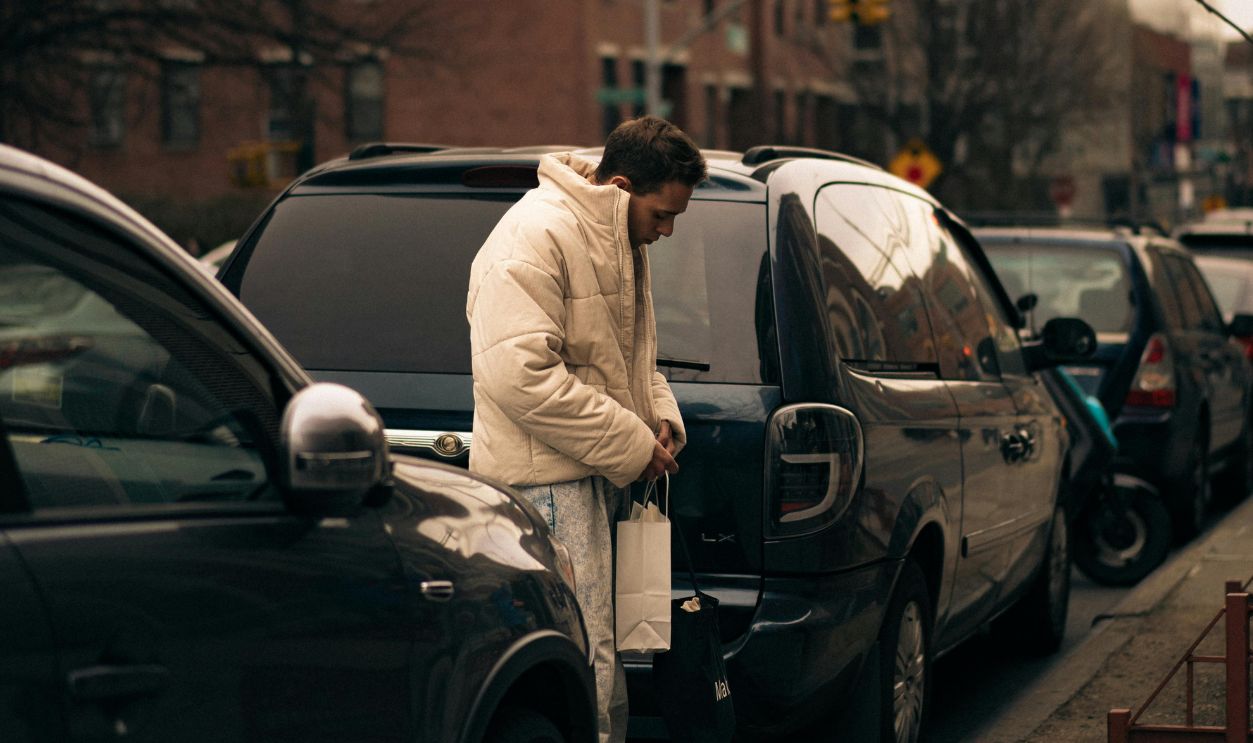 A person in a white jacket stands by parked cars on a city street, capturing urban life