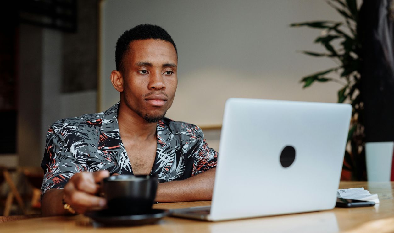 Young man in coffee shop working on laptop with a cup of coffee, modern and relaxed vibe