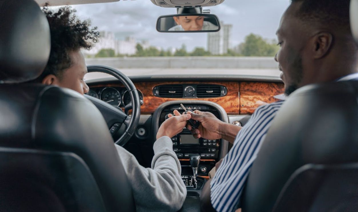Father and teenage son inside car learning to drive, fostering bonding and guidance.