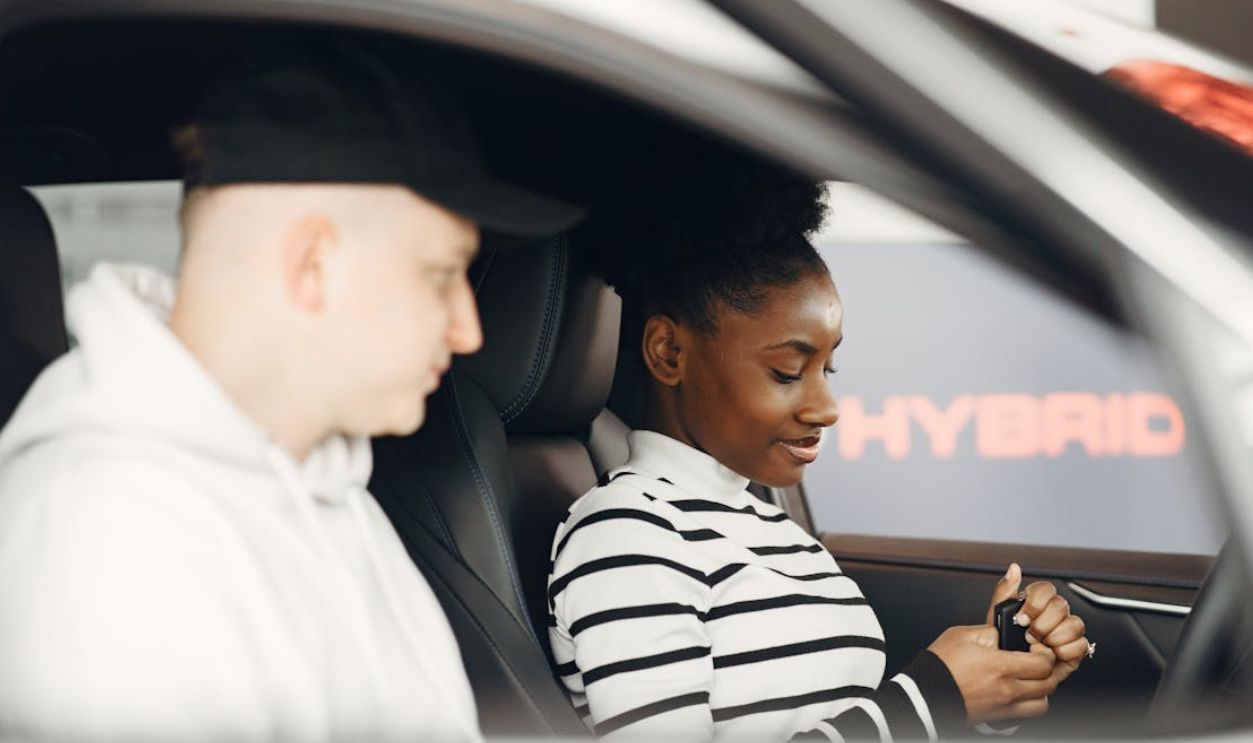 A man and woman sitting inside a hybrid car, discussing its features, highlighting modern eco-friendly transportation.