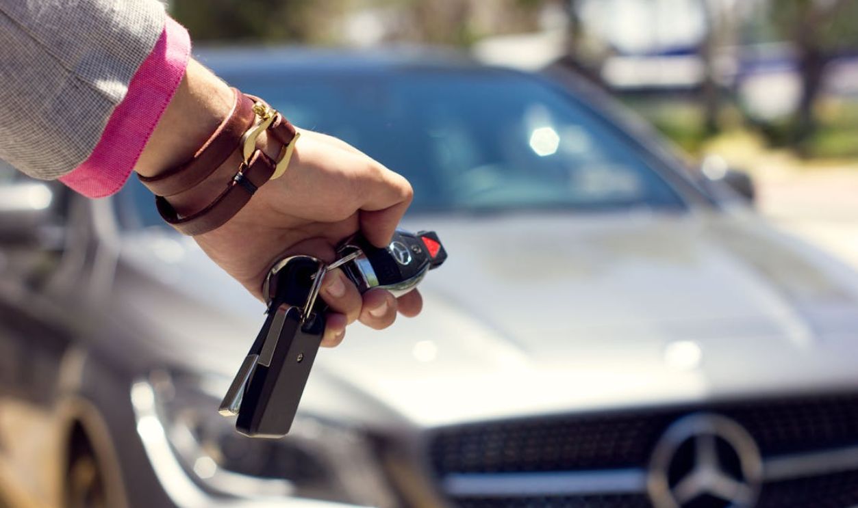 A close-up image of a hand holding car keys against the backdrop of a luxury car, outdoors.