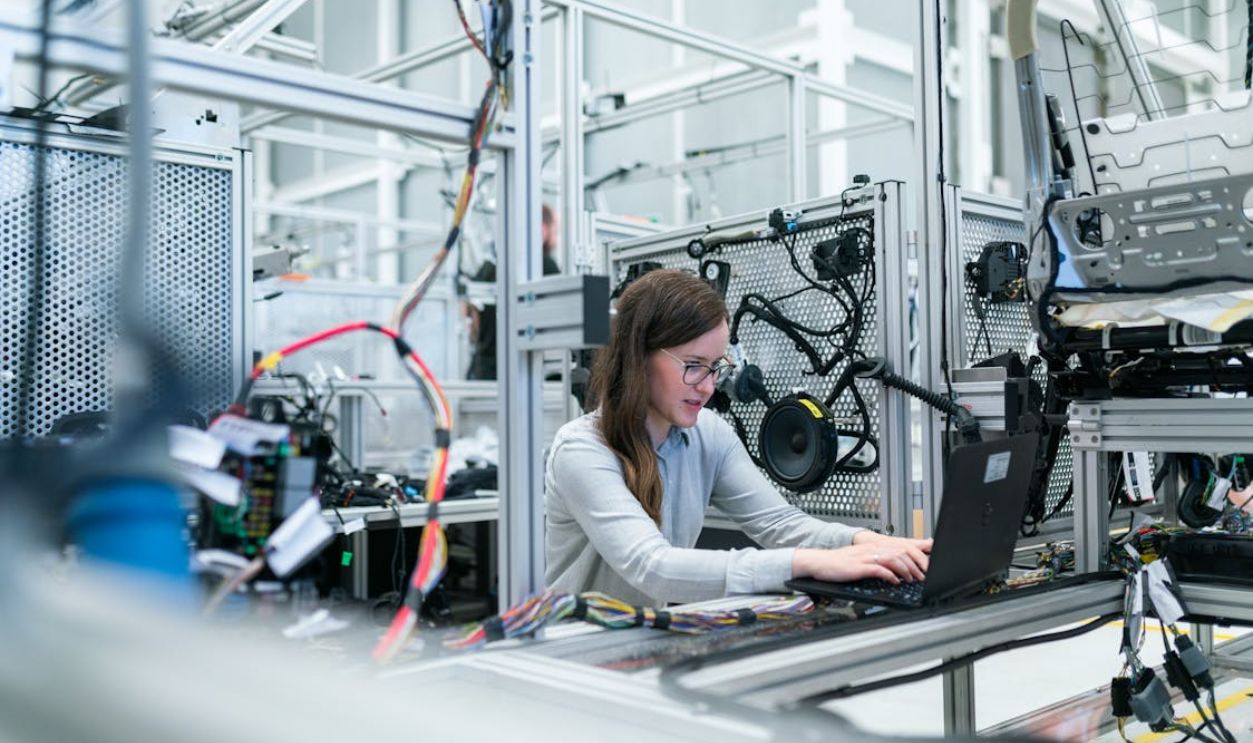 A female engineer focuses on her laptop amidst advanced tech equipment in a lab.