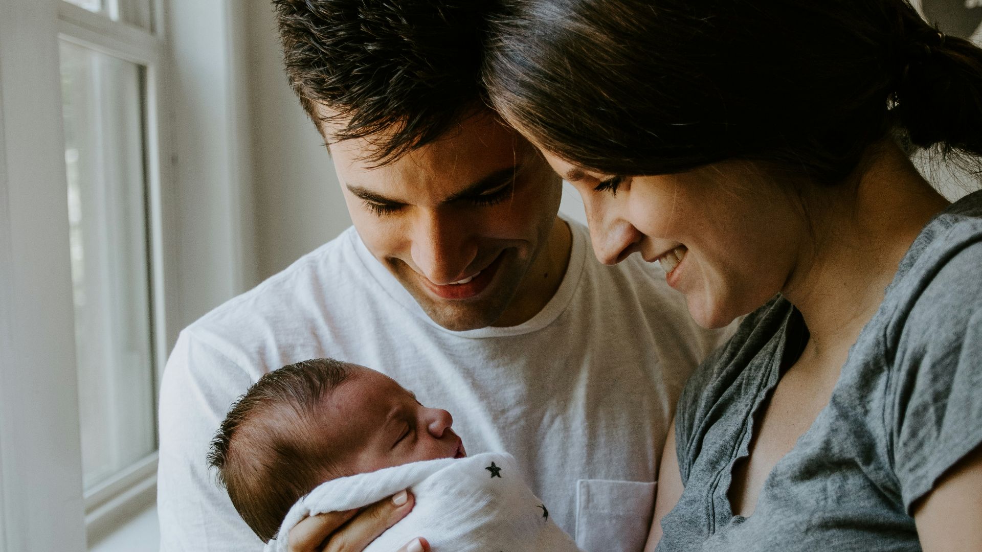 woman holding baby beside man smiling