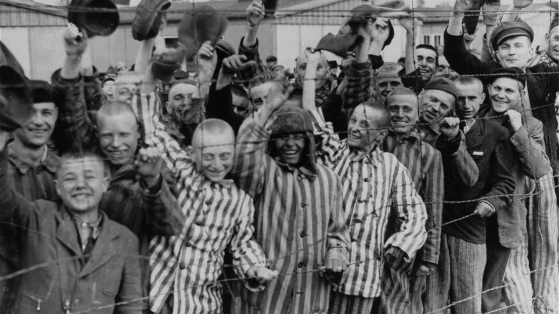 Young and old survivors in Dachau cheer approaching U.S. troops.