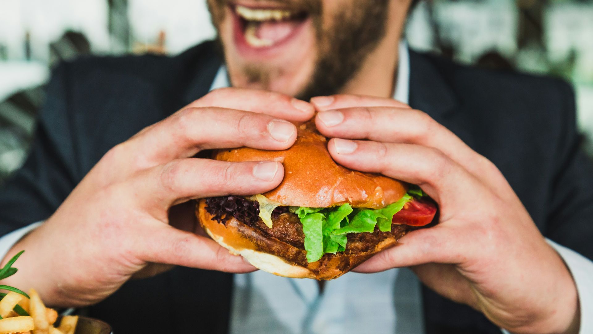person holding burger bun with vegetables and meat