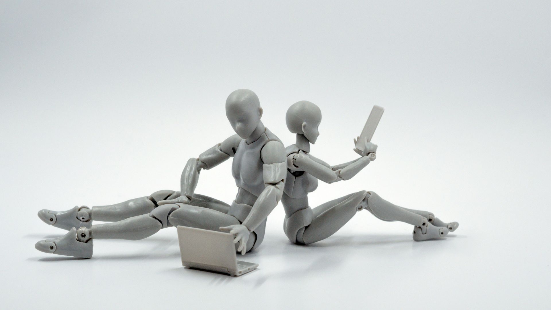 two grey plastic action figures sitting on floor back to back