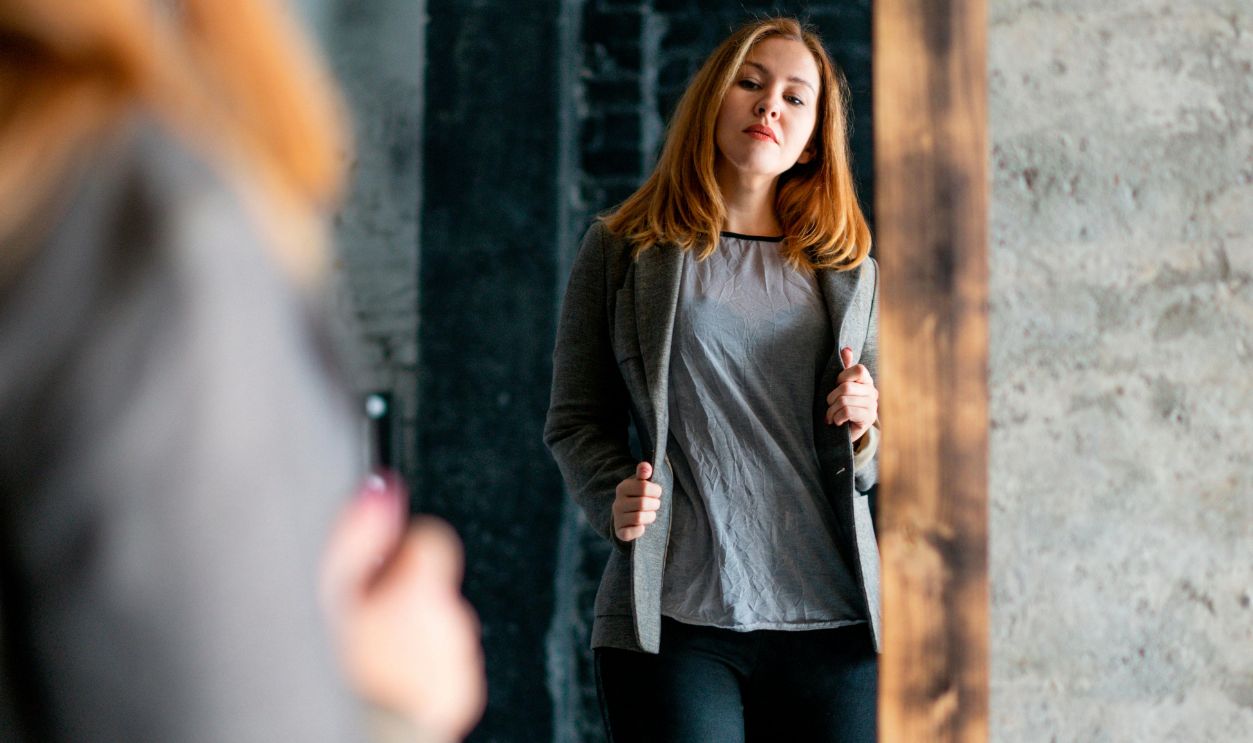 Woman in casual attire checks her look in a large mirror inside a modern room