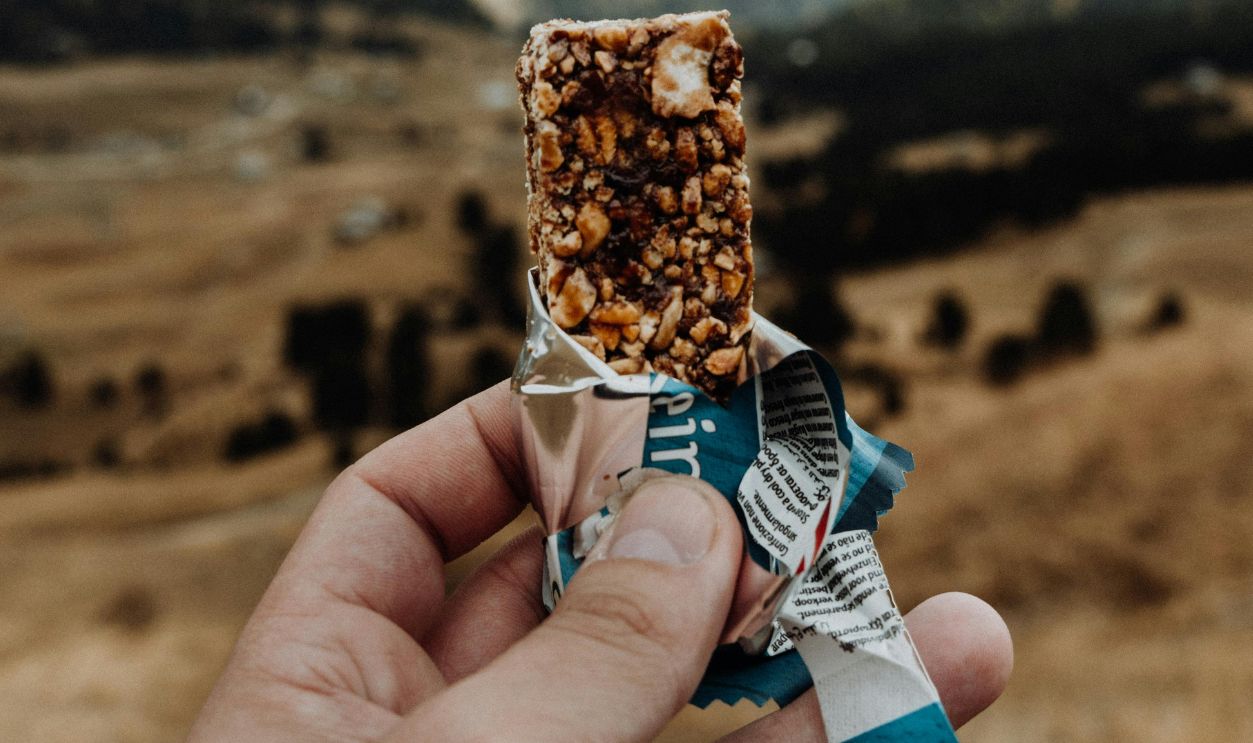 Person holding a cereal bar with a mountainous landscape in Trentino, Italy