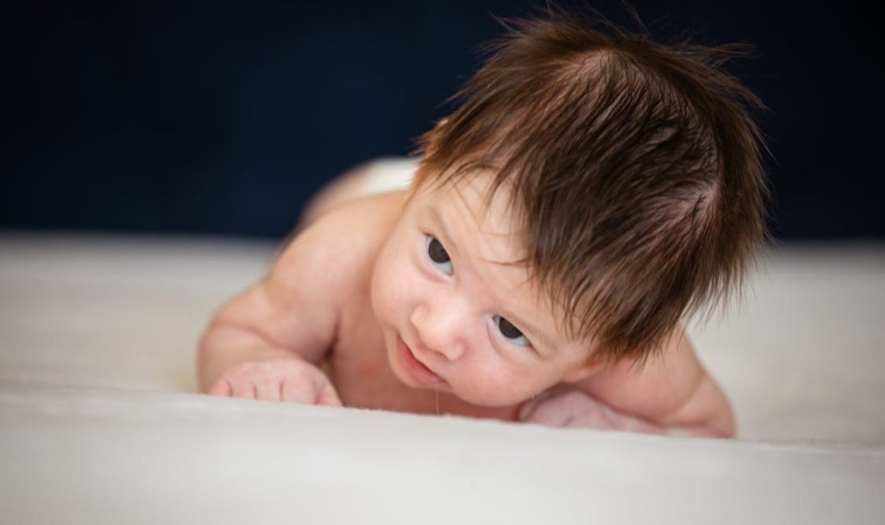 Charming newborn baby boy lying on a soft white blanket, showcasing innocence and cuteness.