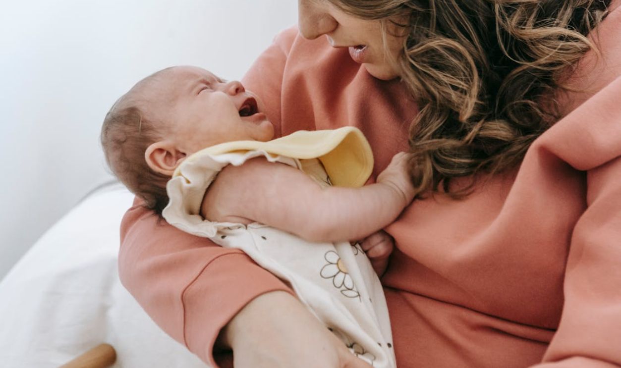 A nurturing mother calms her crying baby in a warm indoor setting, showcasing maternal love.
