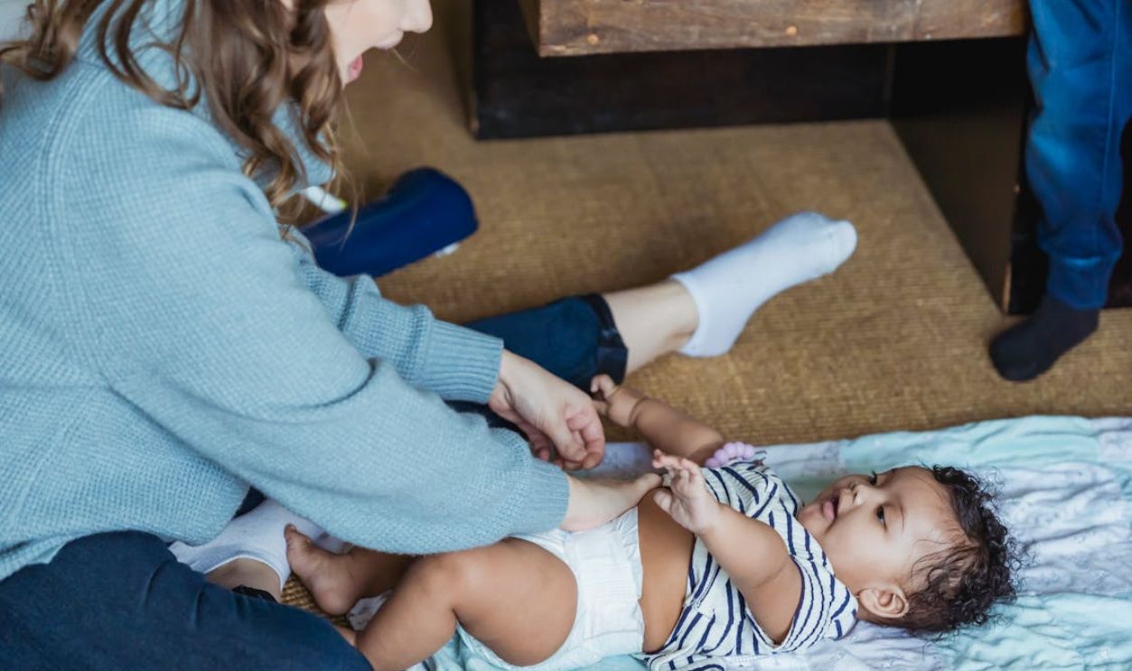 A mother lovingly changes her baby's diaper at home, capturing a moment of tenderness.