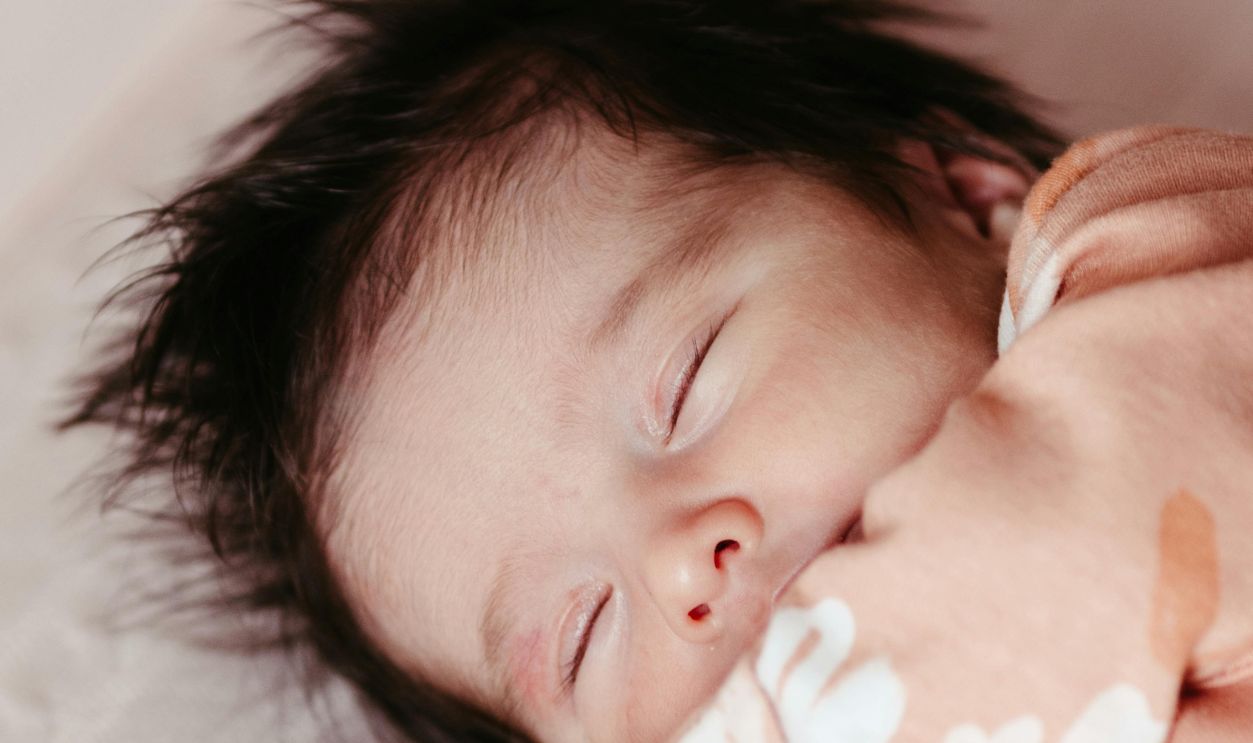 Close-up of a serene Asian baby sleeping in a floral outfit symbolizes innocence and tranquility.