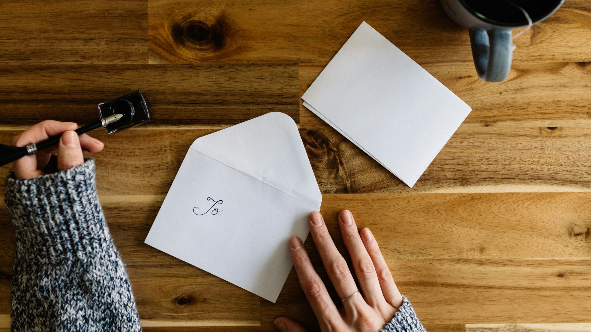 a person writing on a piece of paper next to a cup of coffee