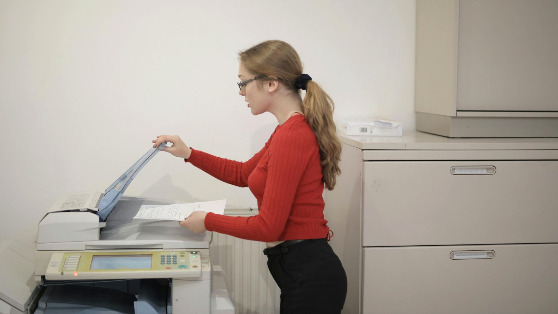 An office employee using a photocopier to copy documents indoors.
