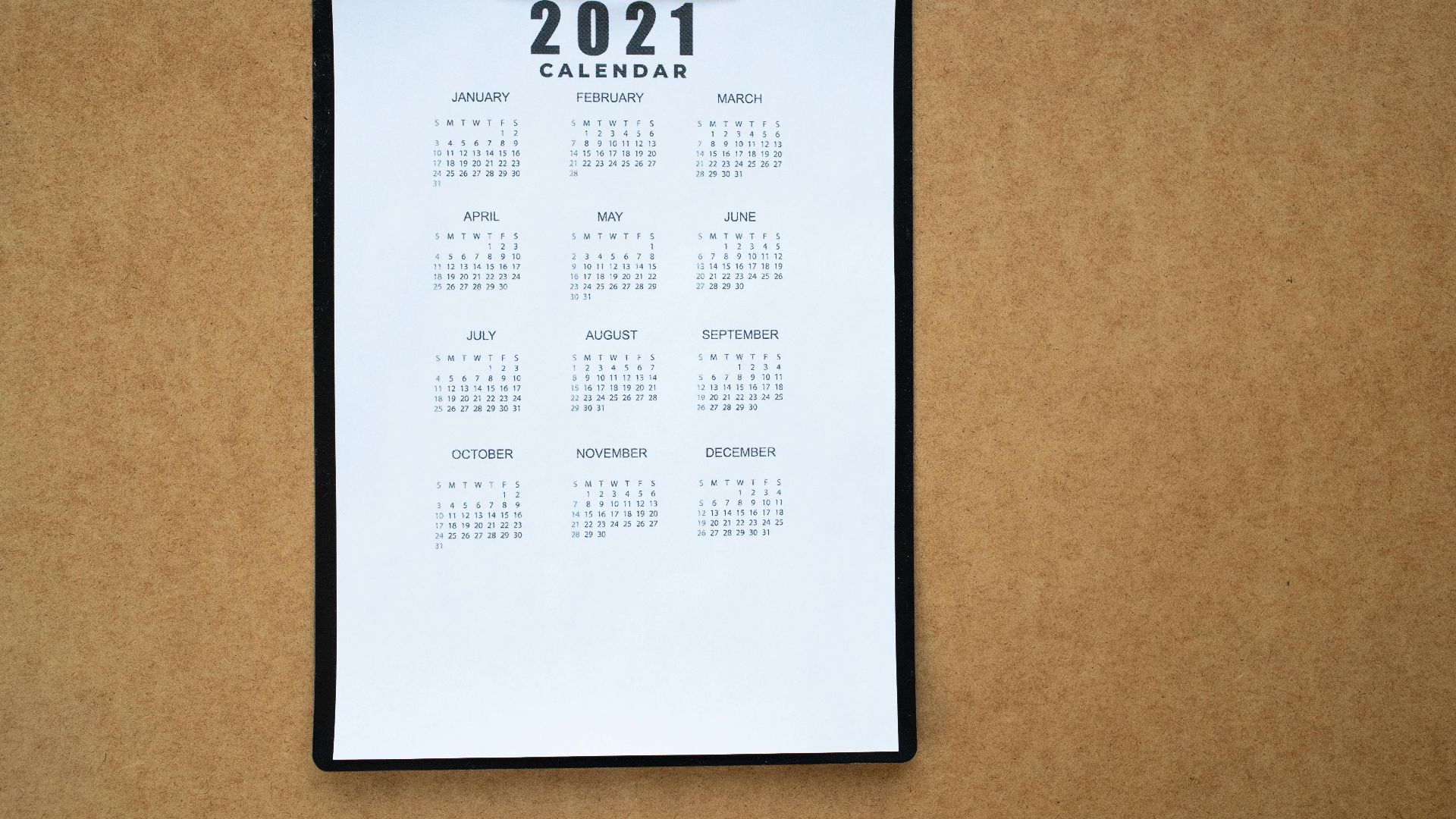 A 2021 calendar clipped to a black clipboard on a brown surface. Ideal for planning or scheduling visuals.
