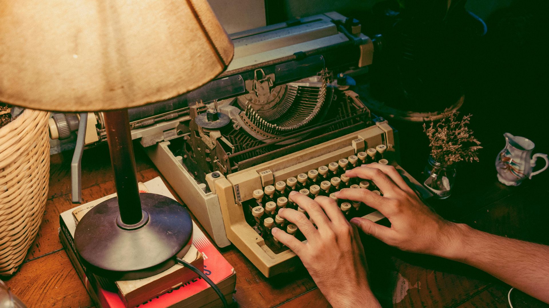 Hands typing on a vintage typewriter under a warm lamp glow, evoking nostalgia.