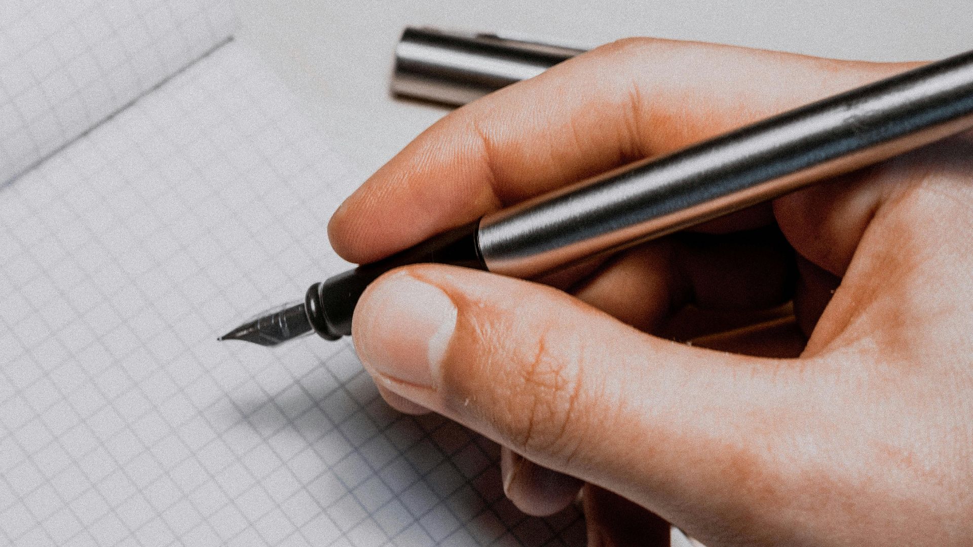 A detailed shot of a hand holding a fountain pen over graphing paper, suggesting creativity and planning.